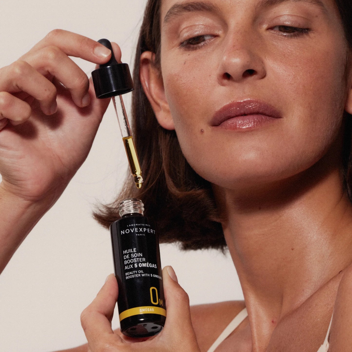 Woman holding a Novexpert beauty oil serum with 5 Omegas dropper bottle -at www.mnmkanak.com