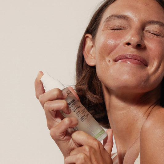 Woman applying Novaexpert Radiance Perfection Mist to her face with a neutral background