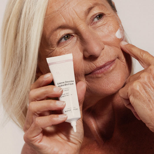 Woman applying cream to her face with a tube of Crème Douceur Hydro Biologique in her hand.