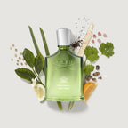 Green Creed perfume bottle surrounded by leaves and citrus fruits on a light background