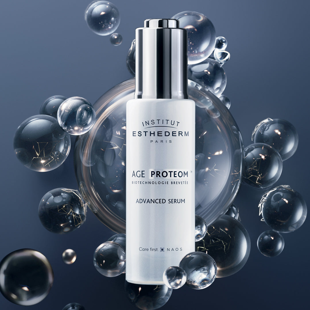A bottle of AGE PROTEOM Advanced Serum by Institut Esthederm, depicted with a background of bubbles and a blue tone, highlighting its skincare properties.