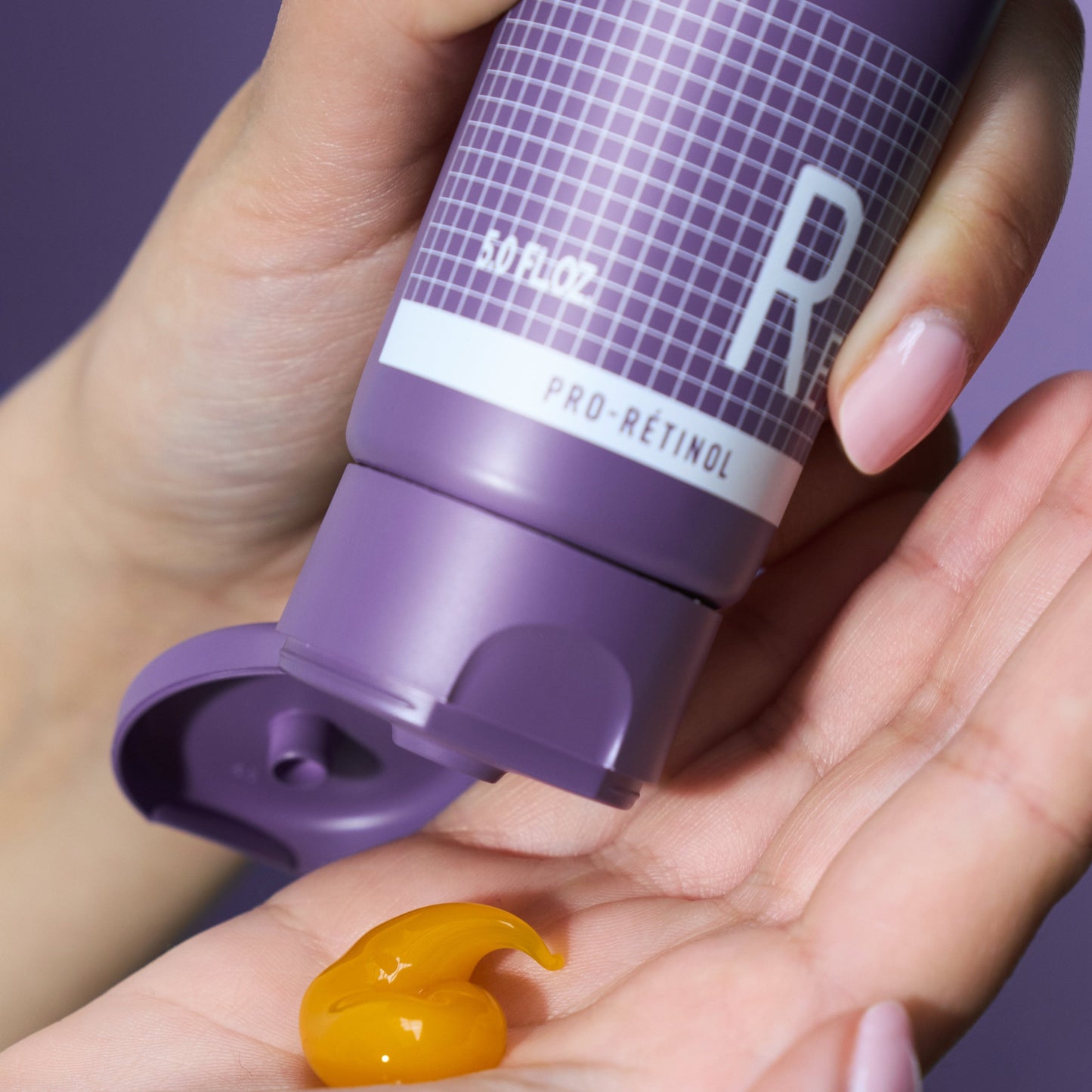 Hand holding a purple skincare product with visible cream on palm against a purple background
