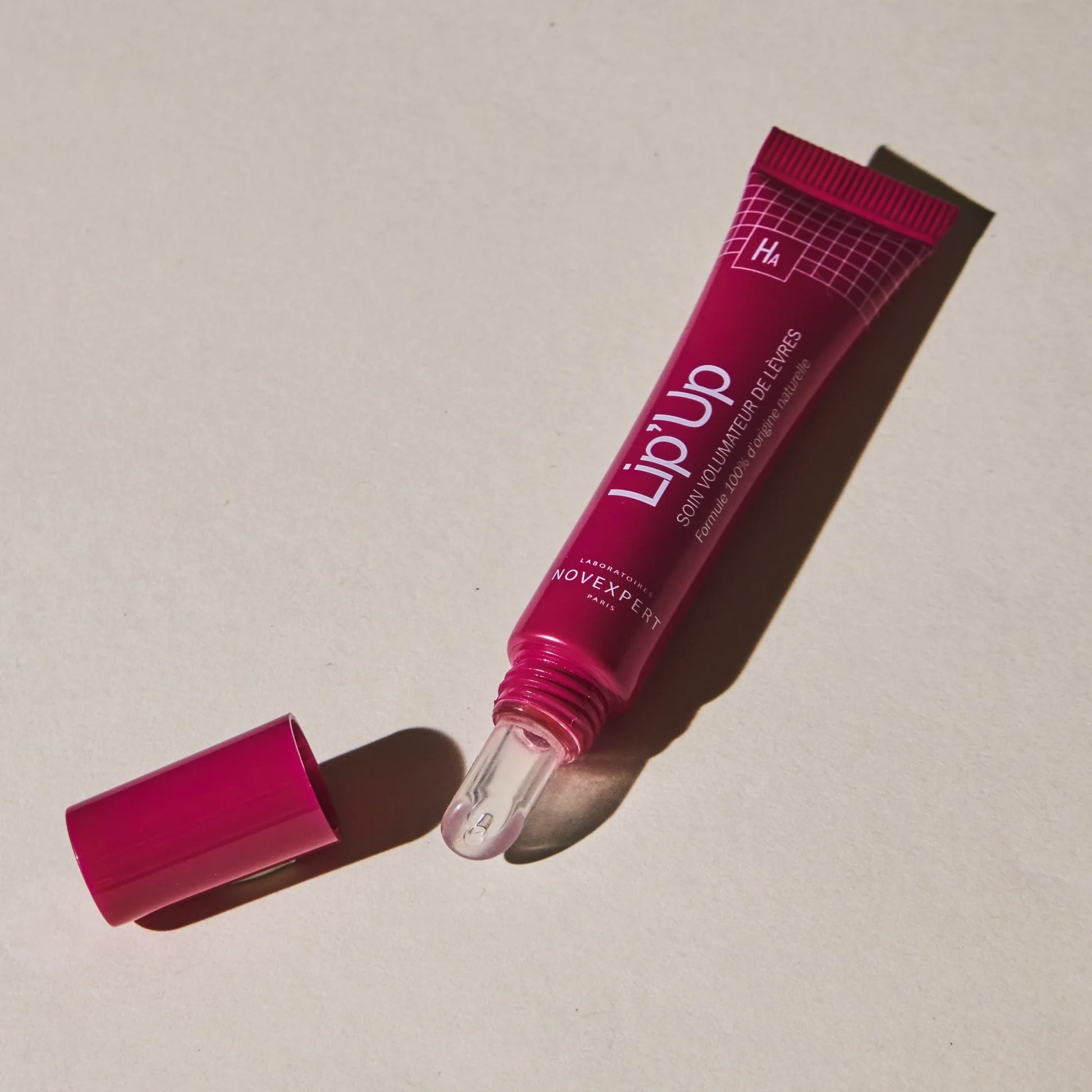 Pink 'Lip'Up' lip balm tube on a beige background