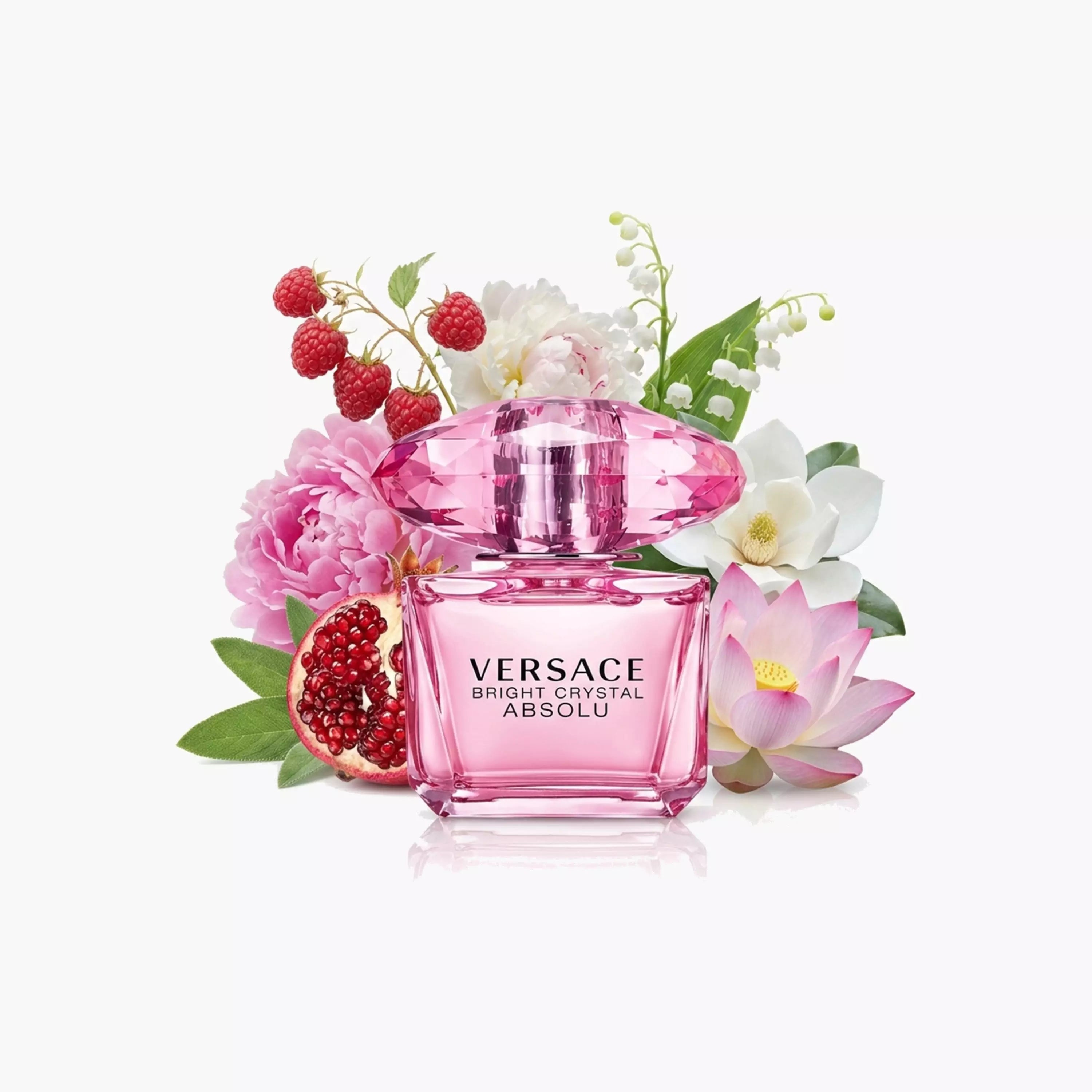 Versace Bright Crystal Absolu perfume bottle in pink, styled with pink flowers, white blossoms, red berries, and a pomegranate on a clean white background.